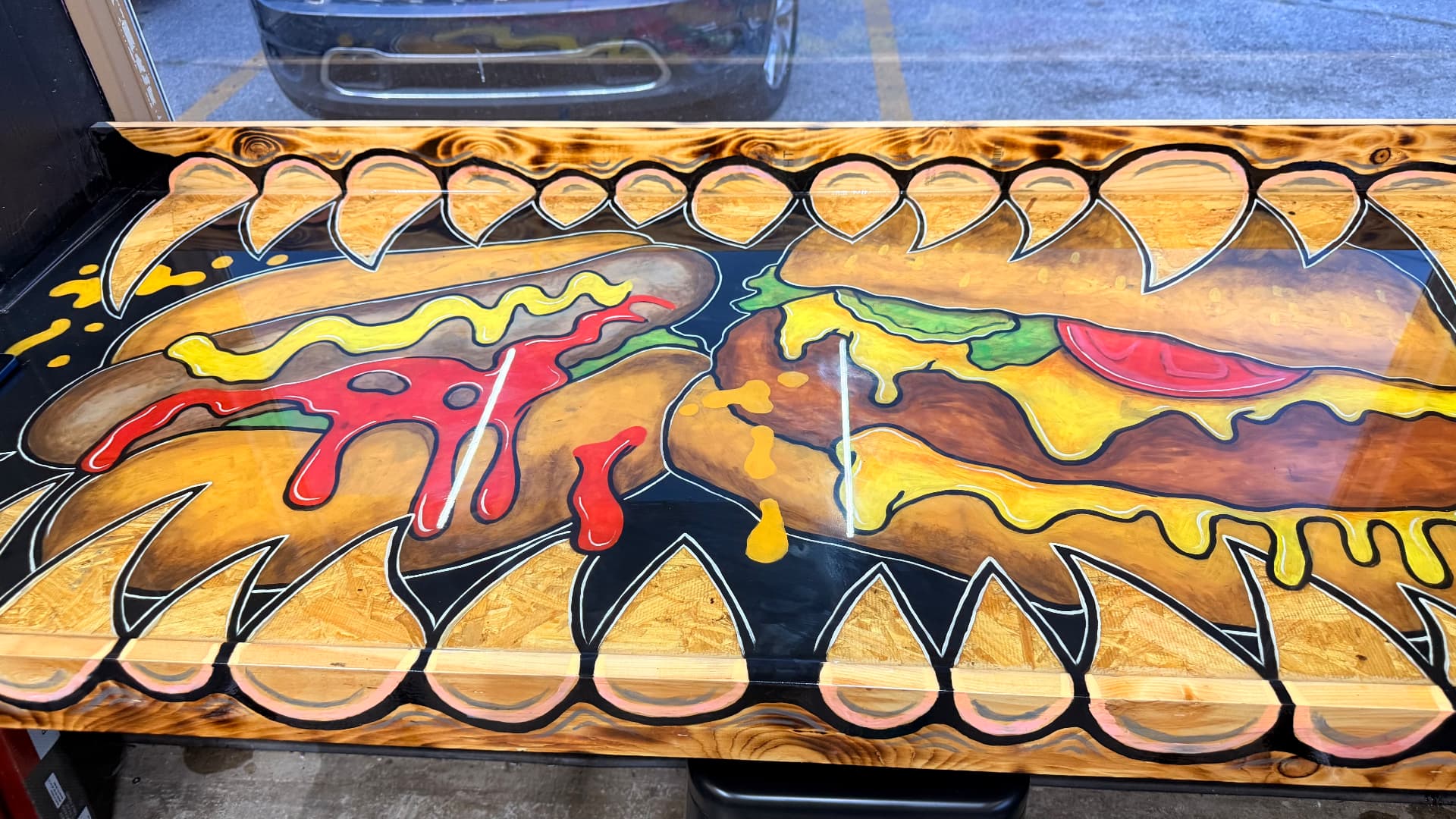 Painted loaded hot dogs with mustard and ketchup drips inside monster teeth on a shop table