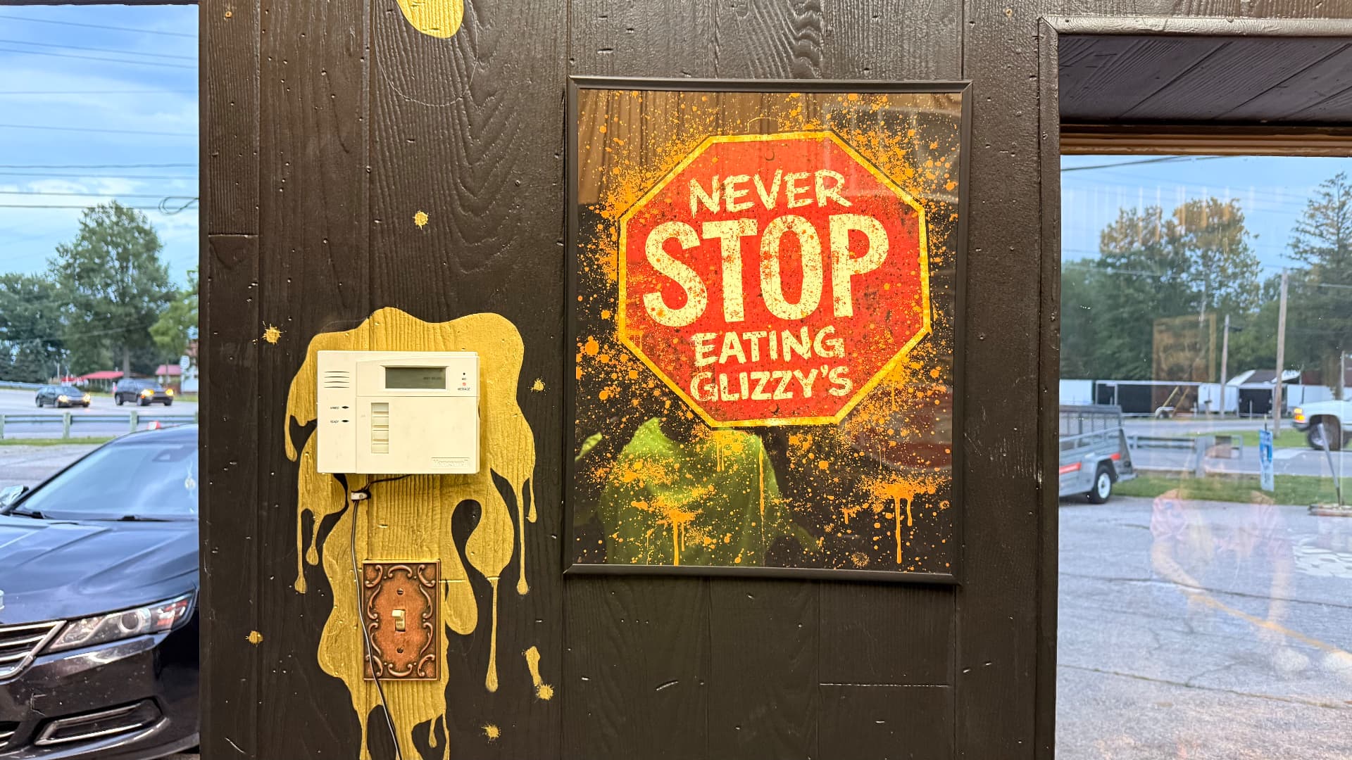 Never Stop Eating Glizzy's framed stop sign poster on the shop wall next to dripping gold paint
