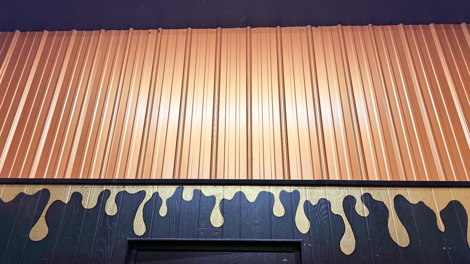 Gold paint drips running down the black shop wall under copper metal siding